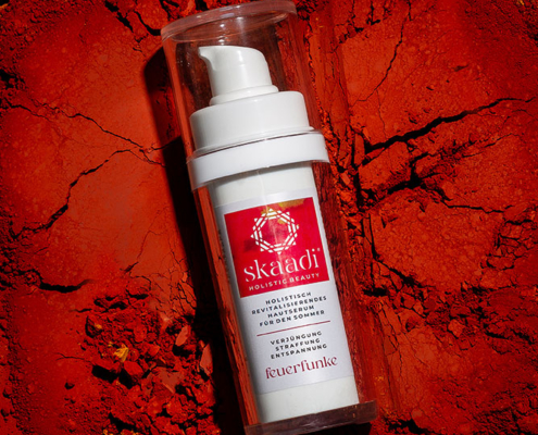 skaadi® Feuerfunke Elementra Sommerserum liegt auf rotorangen pudrigen Untergrund mit Rissen