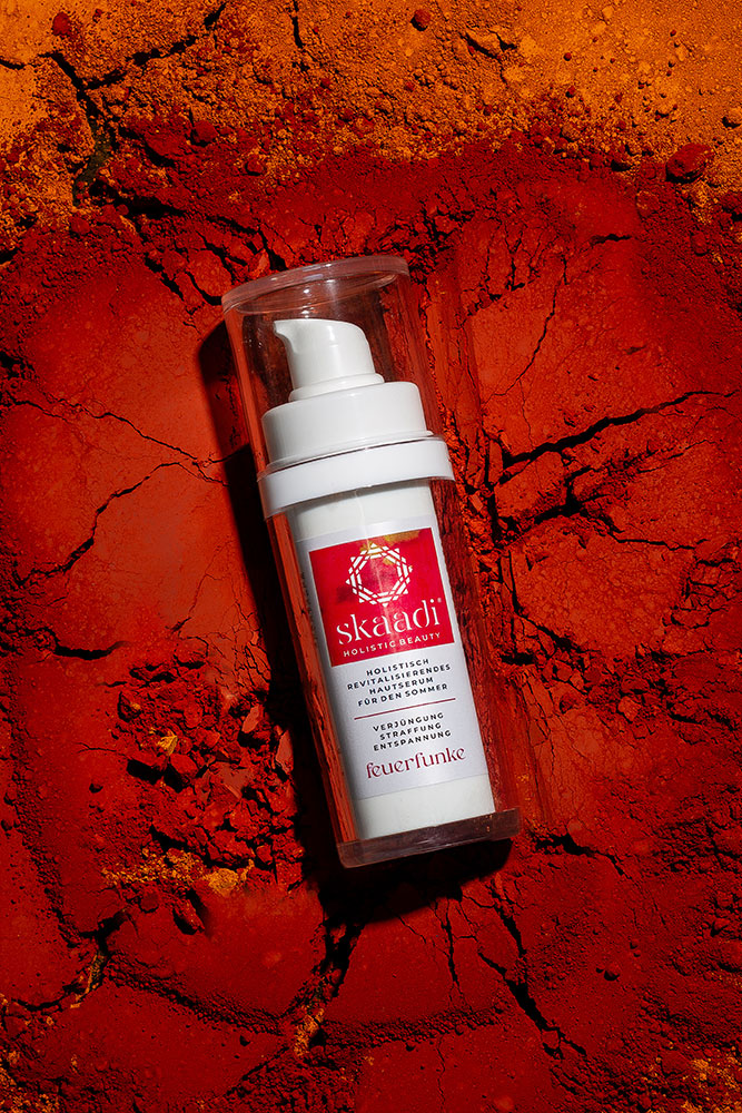 skaadi® Feuerfunke Elementra Sommerserum liegt auf rotorangen pudrigen Untergrund mit Rissen